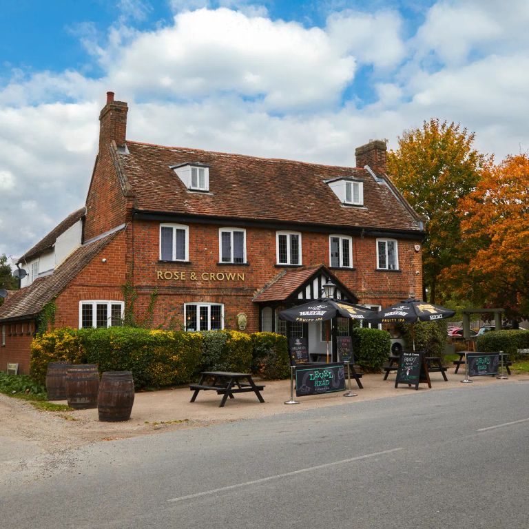 Historic brick pub, Rose & Crown, with outdoor seating, fall foliage, and a cloudy blue sky.